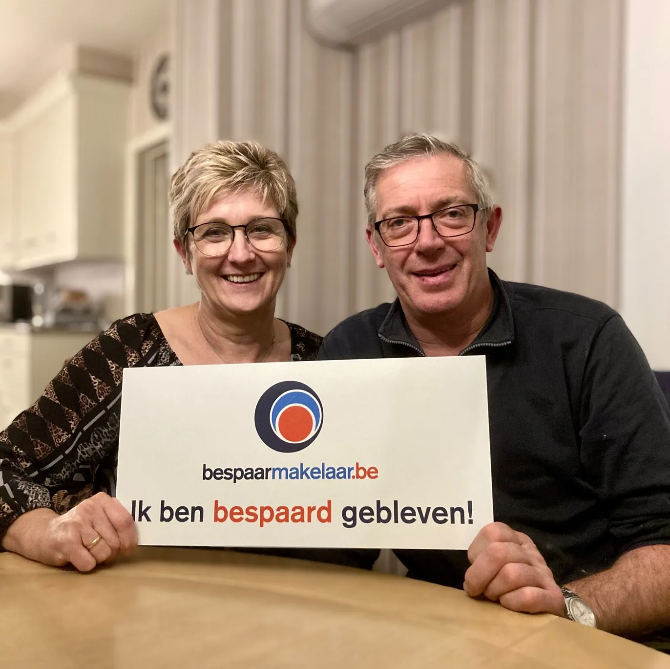 Koppel aan tafel met het bordje 'Ik ben bespaard gebleven!'
