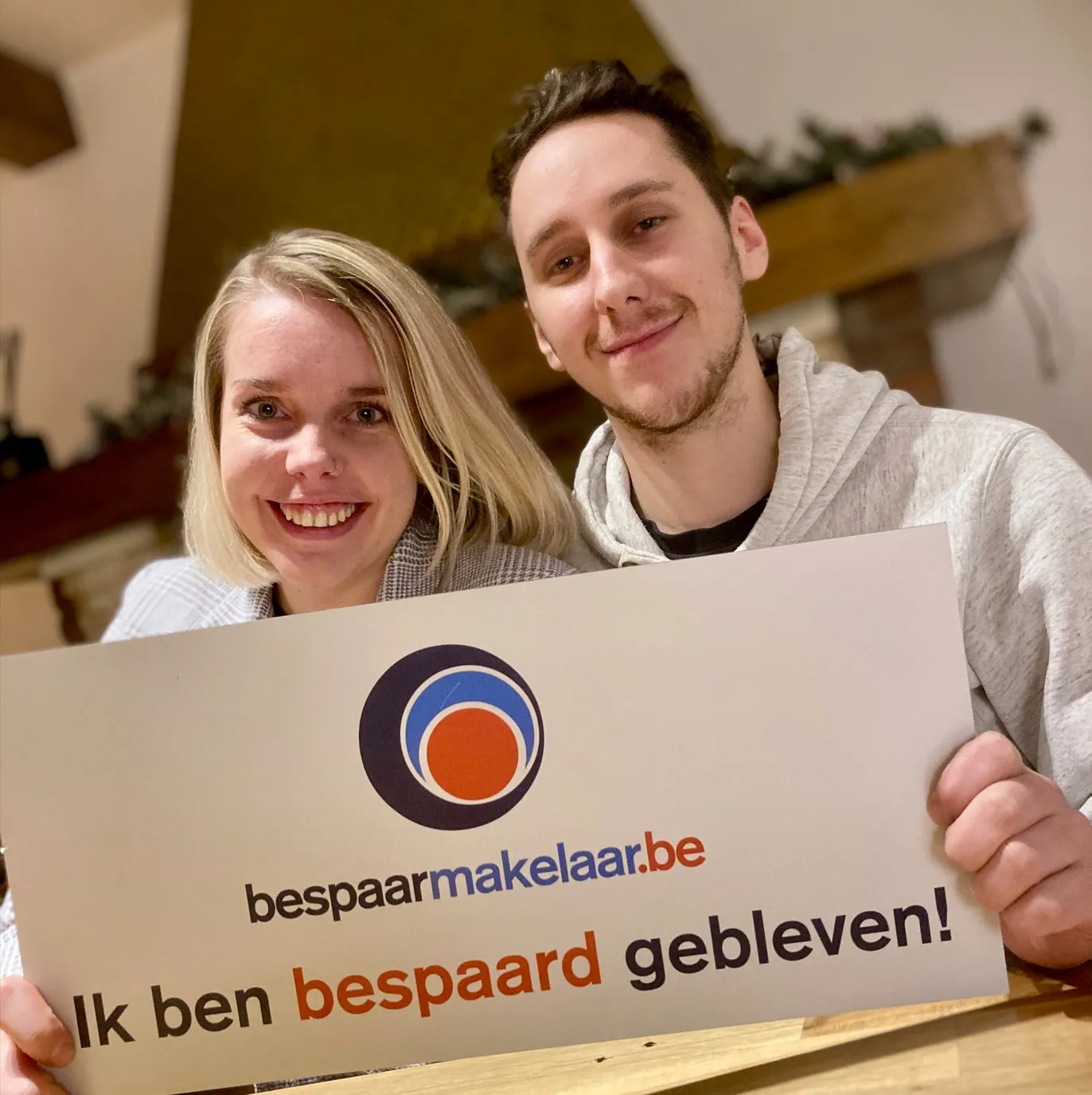 Jong koppel thuis met het bordje 'Ik ben bespaard gebleven!'