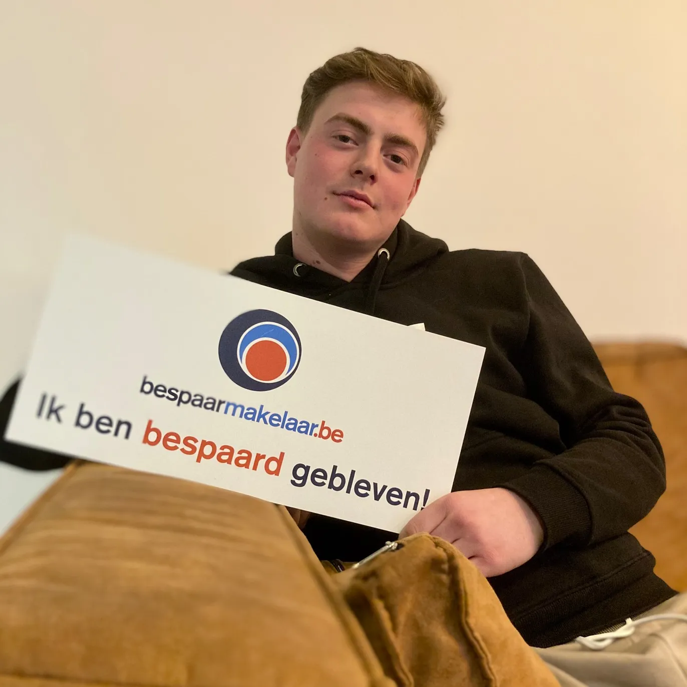 Jonge man in de zetel met het bordje 'Ik ben bespaard gebleven!'