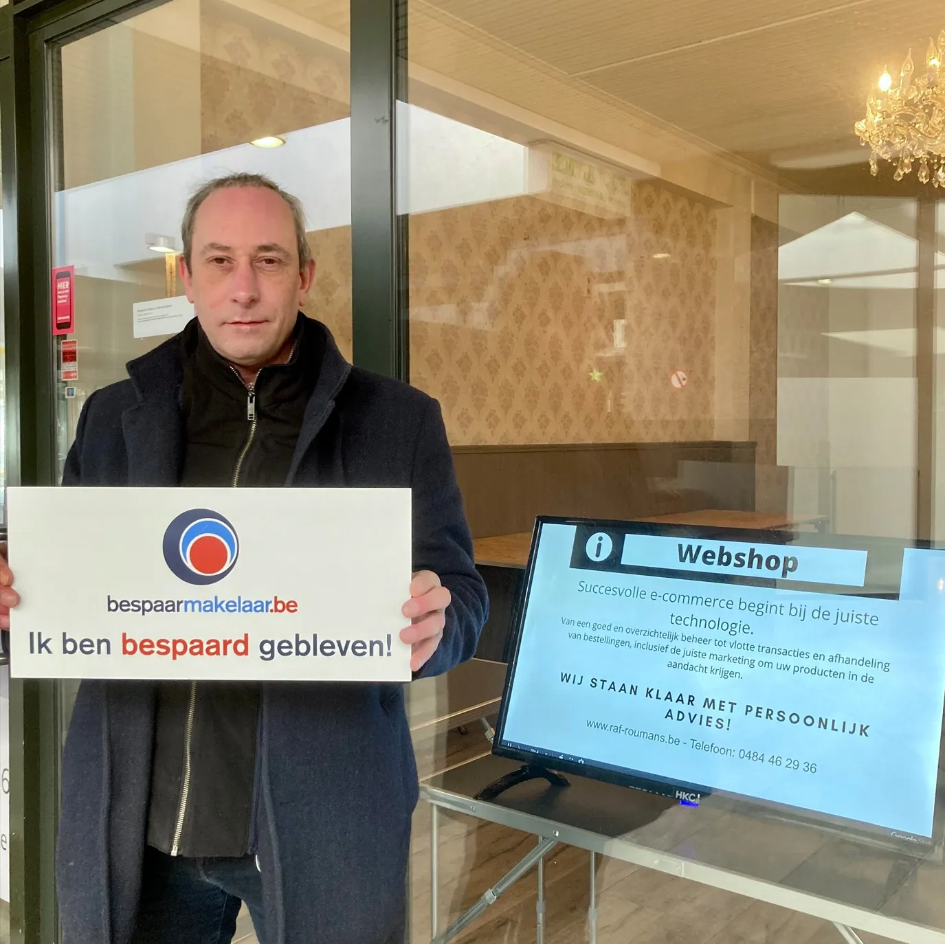 Ondernemer in zijn zaak met het bordje 'Ik ben bespaard gebleven!'