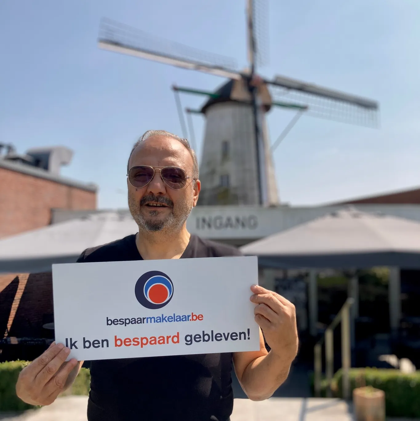 Klant voor een windmolen met het bordje 'Ik ben bespaard gebleven!'